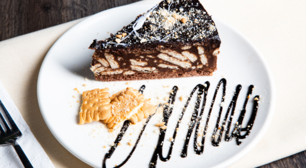 Close up slice of no-bake chocolate biscuit cake showing biscuit chunks and fudgy texture on a rustic ceramic plate.